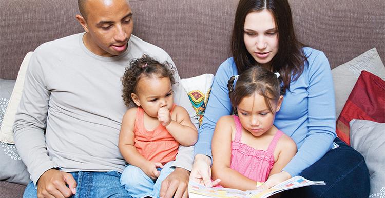 Black adult male and white adult female reading with their children