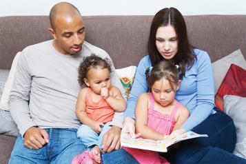 Black adult male with white adult female reading with their children