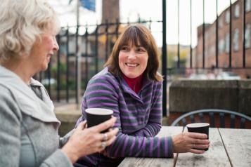 Two women sitting down at a table drinking coffee