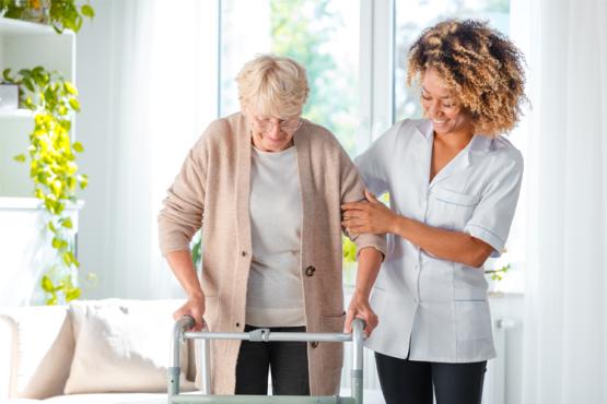Elderly lady with walking frame being supported by a carer